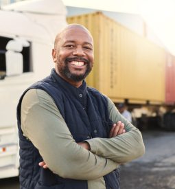 Delivery, container and happy truck driver moving industry cargo and freight at a shipping supply chain or warehouse. Smile, industrial and black man ready to transport ecommerce trade goods or stock.
